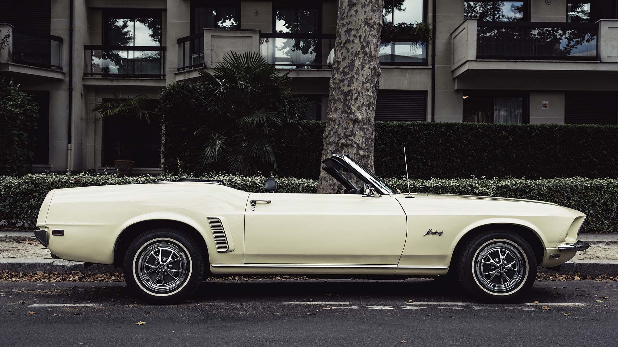 Classic cream-colored convertible parked on a street beside a residential building.