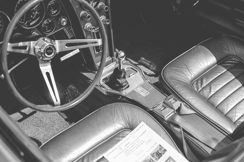 Interior of a classic car with a manual gear shift, three-spoke steering wheel, and leather seats.